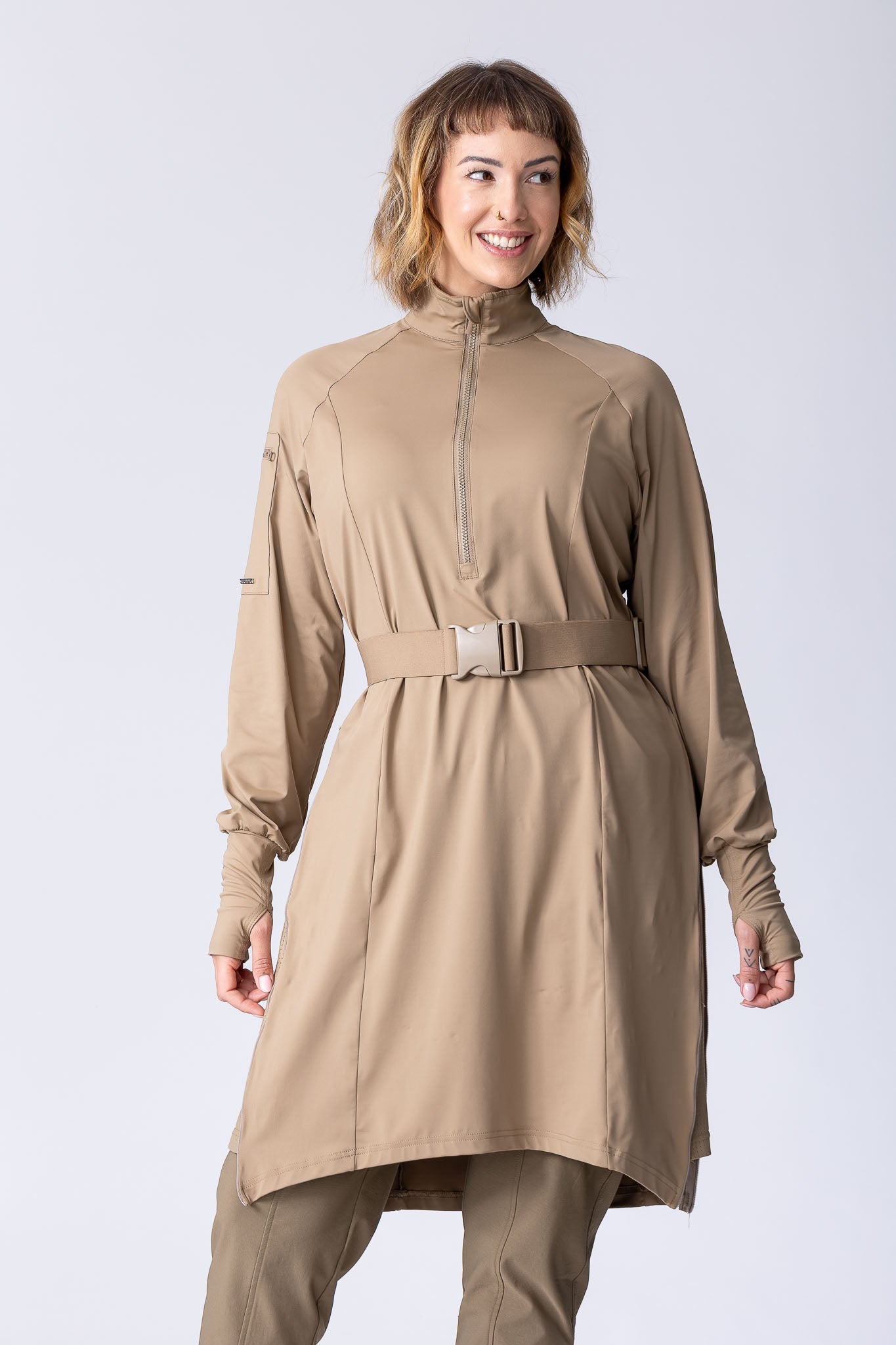 Long line tunic top in beige. With front zipper, hidden side panels, back breathability panel and waist belt with buckle.