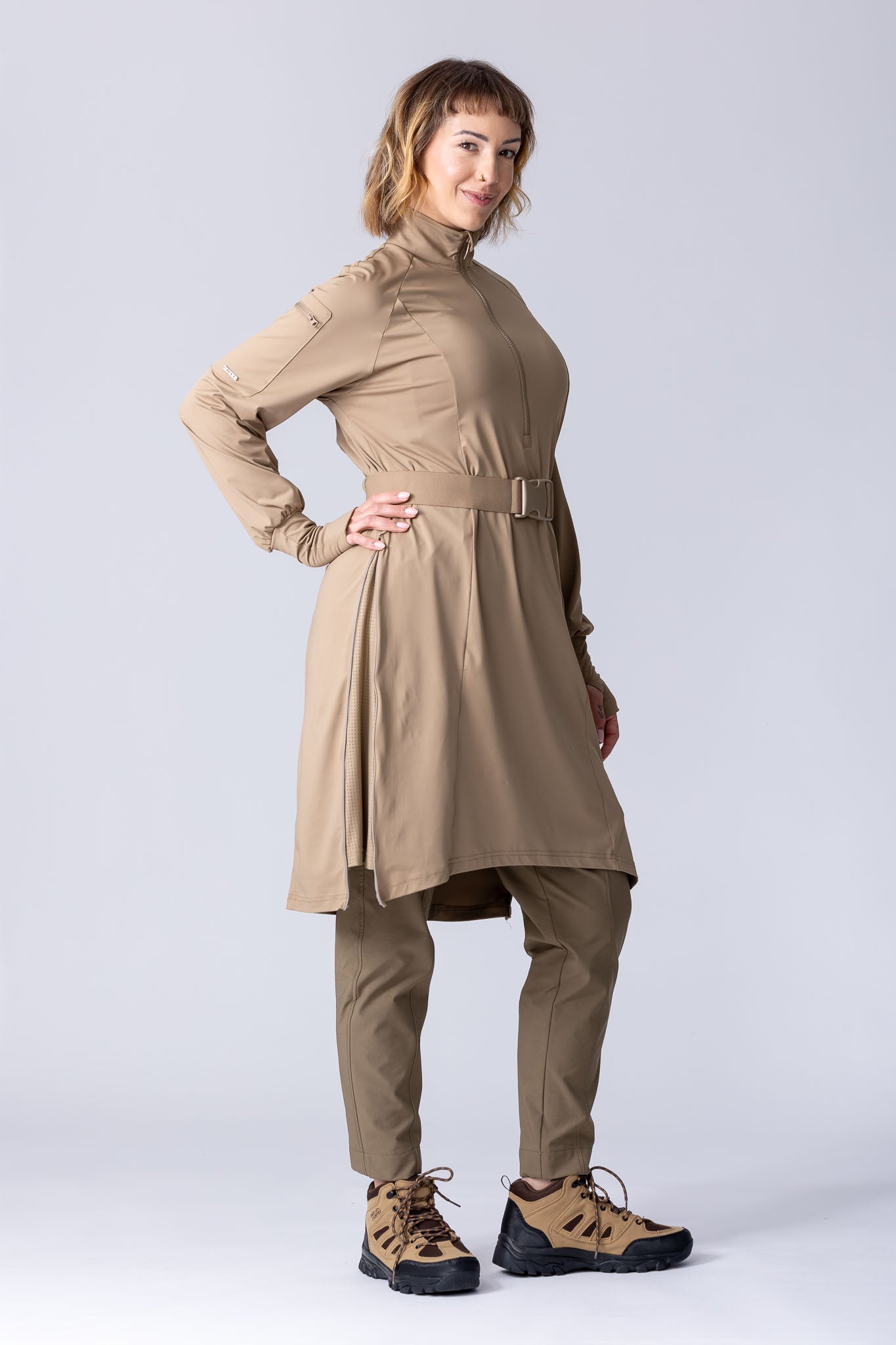 Long line tunic top in beige. With front zipper, hidden side panels, back breathability panel and waist belt with buckle.
