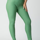 Woman wearing green leggings and a gray t-shirt on a plain background