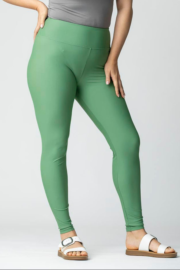 Woman wearing green leggings and a gray t-shirt on a plain background