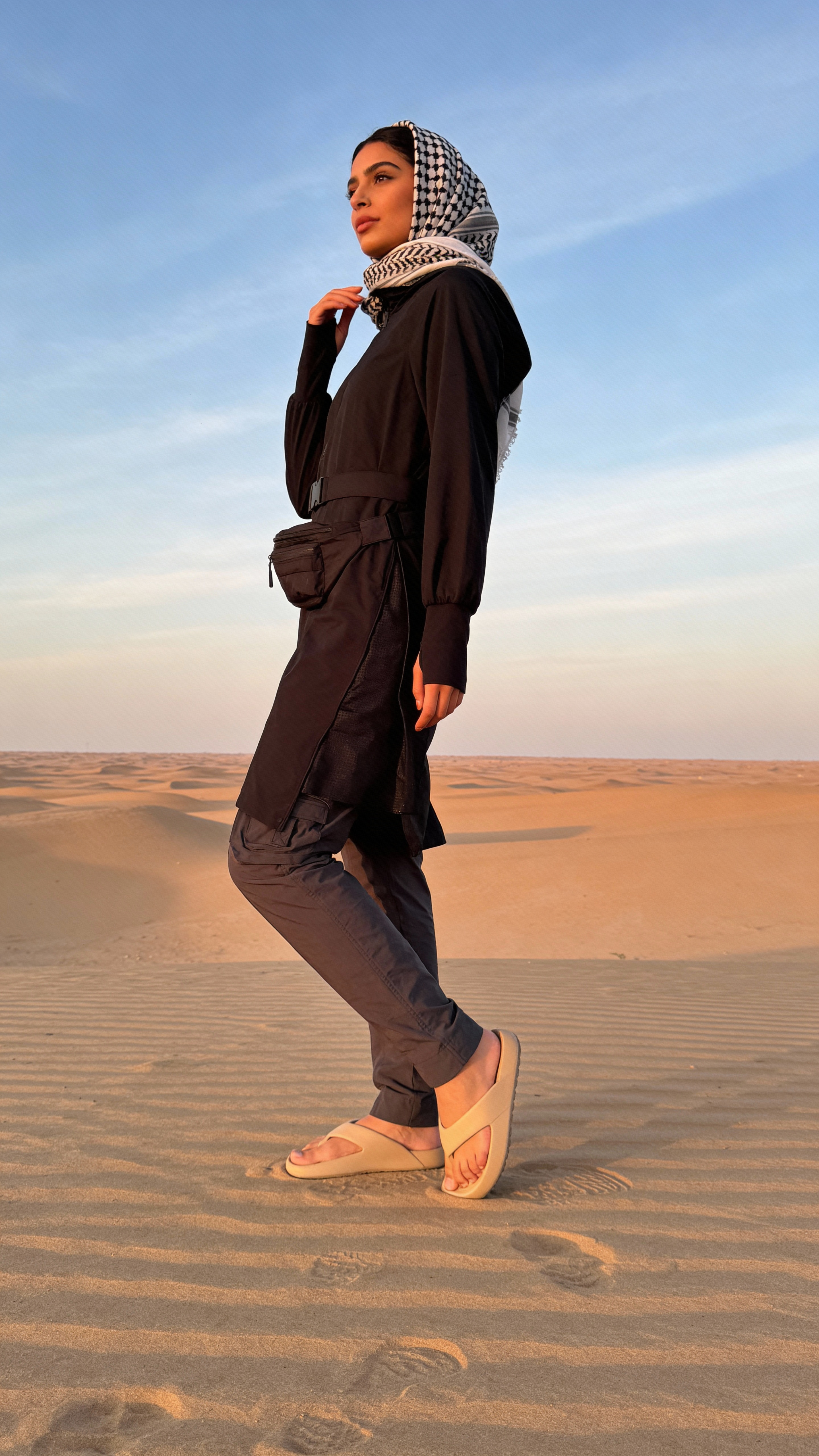 Woman in traditional attire standing on sand dunes with a clear sky