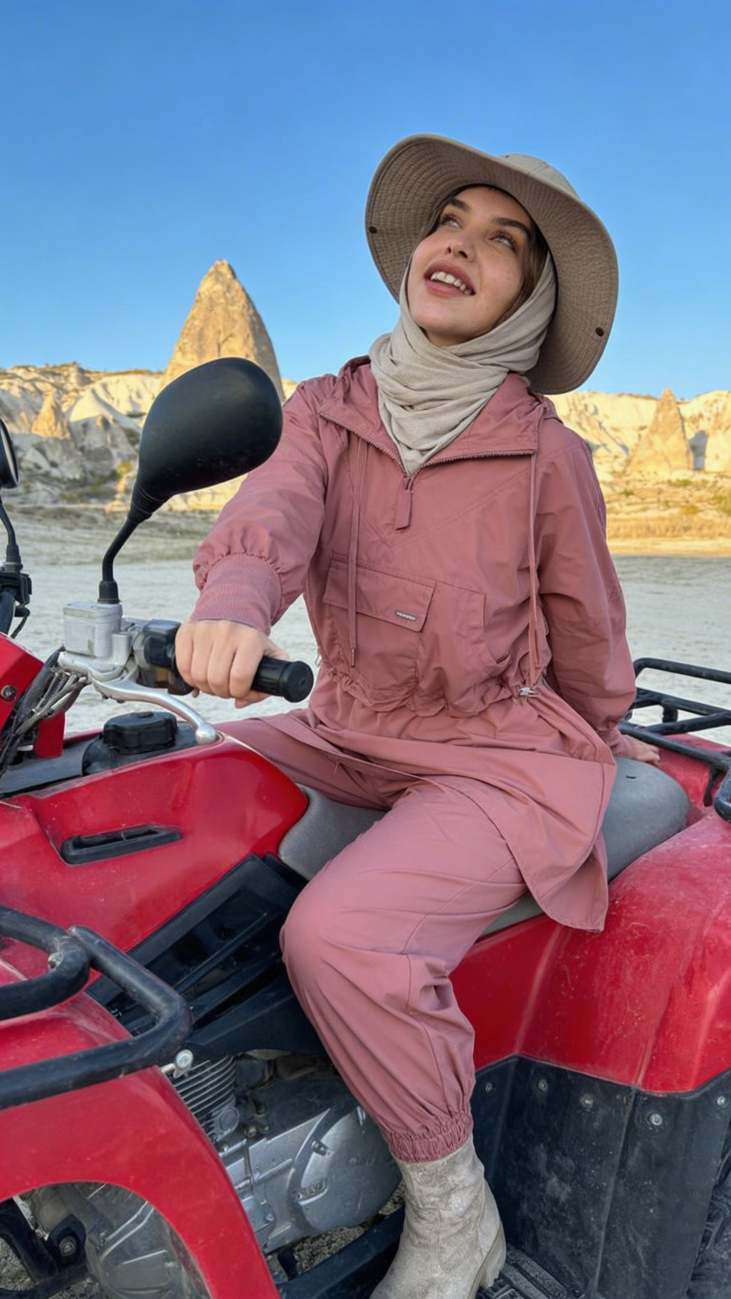 Person in pink outfit and hat sitting on a red ATV with desert landscape in the background